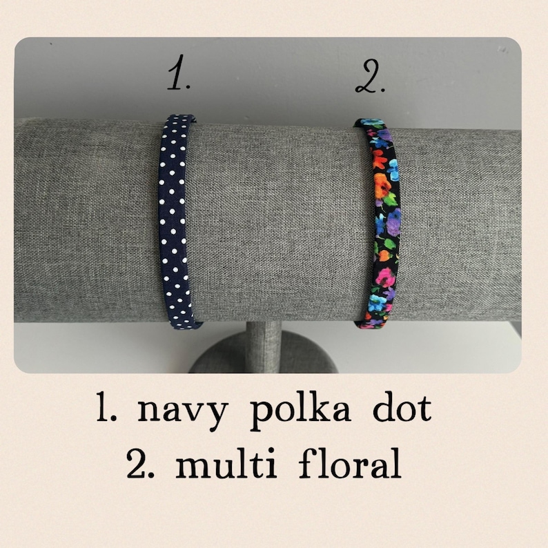 Puede incluir: Dos diademas en un expositor. La diadema de la izquierda es azul marino con lunares blancos. La diadema de la derecha es negra con un estampado floral multicolor. El texto "1. navy polka dot" y "2. multi floral" est&aacute; debajo de las diademas.