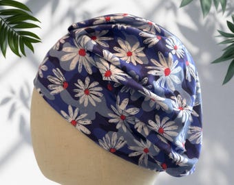 Könnte beinhalten: Eine blaue Mütze mit einem sich wiederholenden Muster aus weißen Gänseblümchen mit roten Mitten. Der Stoff hat eine weiche, geraffte Textur und wird auf einem Schaufensterpuppenkopf präsentiert, wobei der Blumendruck auf der gesamten Oberfläche zu sehen ist.