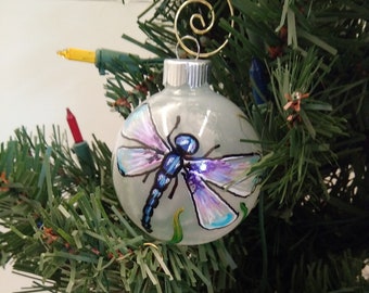 May include: Two glass Christmas ornaments with hand-painted dragonfly designs. The top ornament features a blue and purple dragonfly with green accents. The bottom ornament has a green and blue dragonfly design.