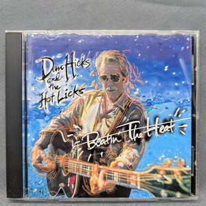 Puede incluir: Caja de CD con el álbum "Beatin' The Heat" de Dan Hicks and the Hot Licks. La portada muestra a un hombre tocando la guitarra con un fondo azul y blanco. El título del álbum está escrito en una fuente estilizada.