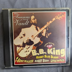 May include: A compact disc case featuring the album More Treasures from the Vault by B.B. King. The cover art displays a musician playing an electric guitar with text listing artists including Bobby Blue Bland, T-Bone Walker, Bobby Rush, and Little Joe Blue.