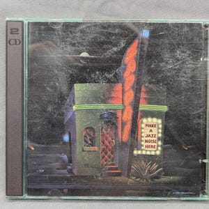 May include: CD case featuring a neon sign that reads "Zappa's" above a building with a red door. The sign "Make a Jazz Noise Here" is also visible. The artwork has a dark, atmospheric style with a surreal quality.