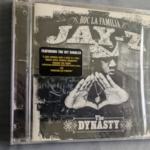 Puede incluir: CD sellado del álbum de Jay-Z, "The Dynasty: Roc La Familia". La portada es en blanco y negro, con Jay-Z con las manos juntas. El título del álbum y el nombre del artista se muestran de forma destacada, junto con una pegatina que enumera los sencillos exitosos.