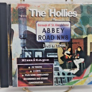 May include: A CD case featuring "The Hollies at Abbey Road N.W.8" with text indicating the years 1963 to 1966. The cover includes a photo of the band performing and details about the tracks, hits, and unreleased recordings.