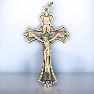 Peut inclure: Un pendentif en métal doré en forme de crucifix avec une figure détaillée de Jésus-Christ sur la croix. La croix a un design décoratif avec une bannière qui dit "INRI".