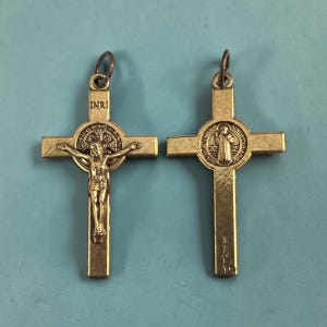 May include: Two gold-colored metal crucifix pendants. One features a depiction of Jesus Christ on the cross, with the letters "INRI" above. The other pendant has a circular emblem with a figure. Both have a loop for a chain.