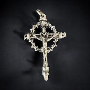 May include: A silver pendant in the shape of a crucifix with a crown of thorns surrounding the figure of Jesus Christ.