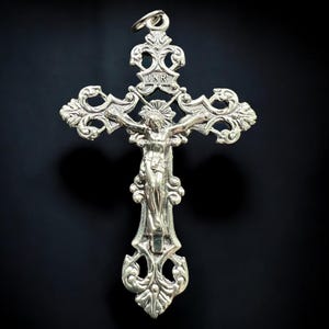 Pode incluir: Pingente de cruz de prata com um design ornamentado e uma figura de Jesus Cristo na cruz. A inscri&ccedil;&atilde;o "INRI" &eacute; vis&iacute;vel no topo da cruz.