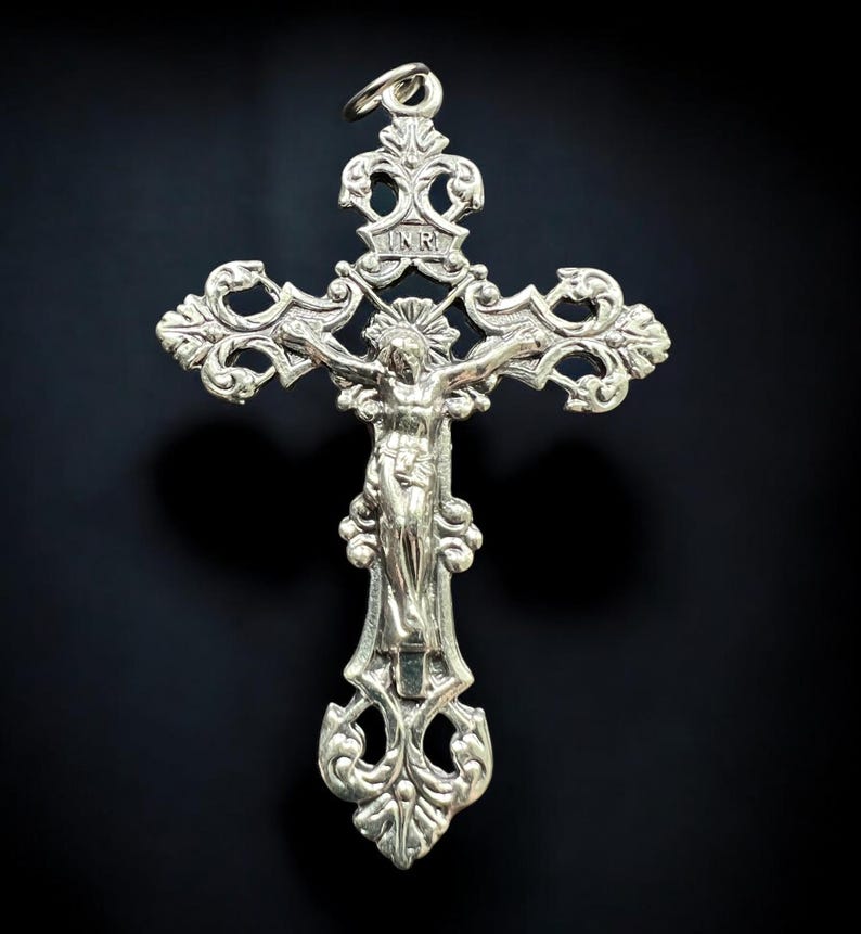 Pode incluir: Pingente de cruz de prata com um design ornamentado e uma figura de Jesus Cristo na cruz. A inscri&ccedil;&atilde;o "INRI" &eacute; vis&iacute;vel no topo da cruz.