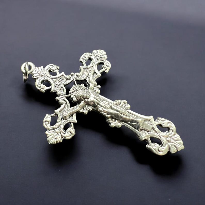 Pode incluir: Um pingente de prata em forma de crucifixo com um design ornamentado. O crucifixo apresenta uma figura detalhada de Jesus Cristo na cruz.