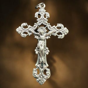 Pode incluir: Um pingente de prata em forma de crucifixo com um design ornamentado e uma figura de Jesus Cristo na cruz. A inscri&ccedil;&atilde;o "INRI" &eacute; vis&iacute;vel na cruz.
