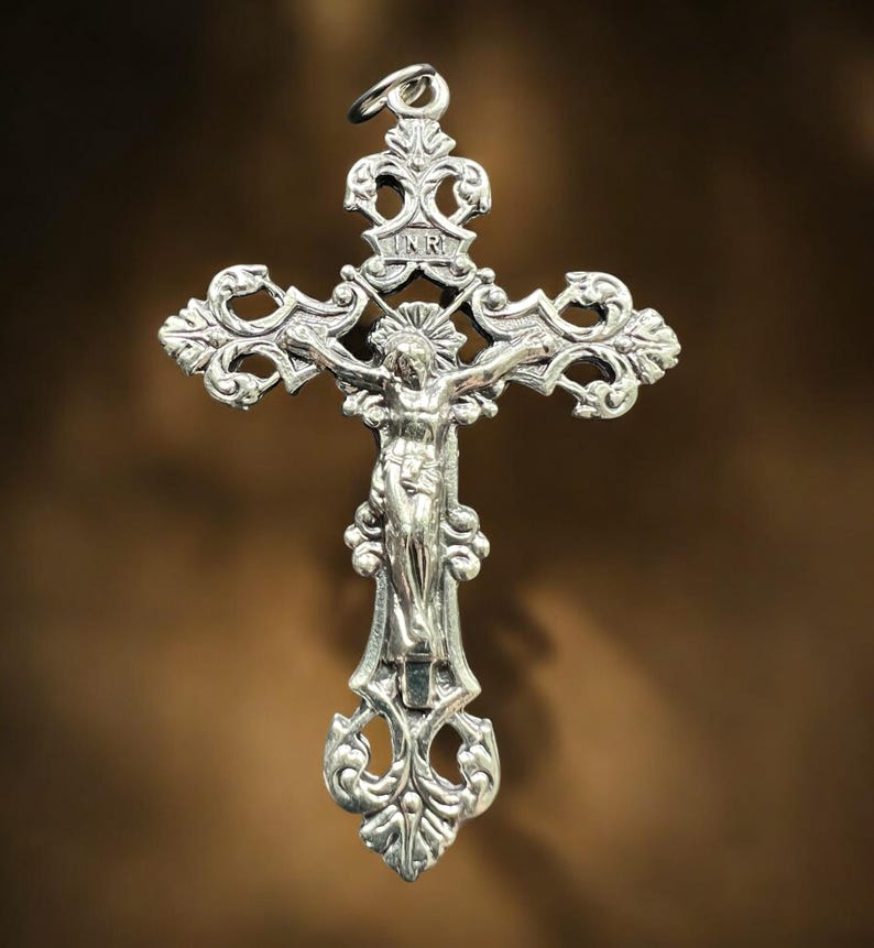 Pode incluir: Um pingente de prata em forma de crucifixo com um design ornamentado e uma figura de Jesus Cristo na cruz. A inscri&ccedil;&atilde;o "INRI" &eacute; vis&iacute;vel na cruz.