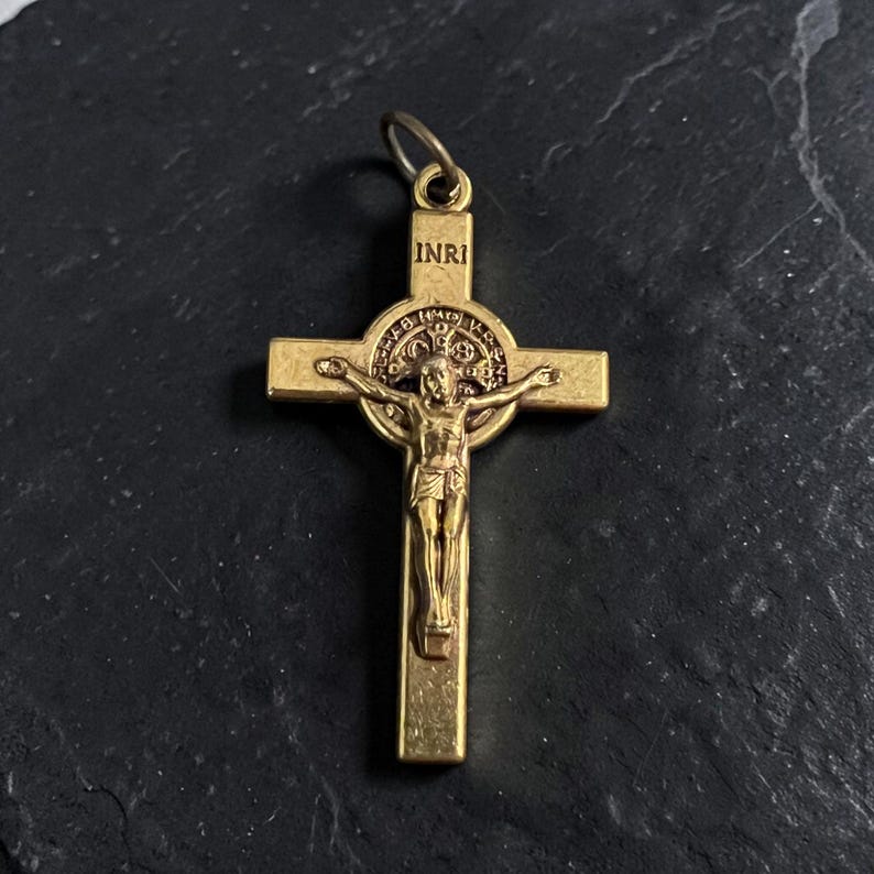 May include: A gold-colored crucifix pendant with the inscription "INRI" at the top. The cross features a detailed depiction of Jesus Christ. The pendant is designed with a loop for easy attachment to a chain or necklace.