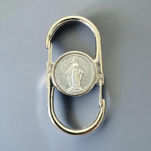 May include: Silver-toned metal keychain with a round charm featuring a depiction of the Virgin Mary. The charm has the text "OUR LADY CONCEIVED WITHOUT SIN PRAY FOR US WHO HAVE RECOURSE TO THEE" around the image.