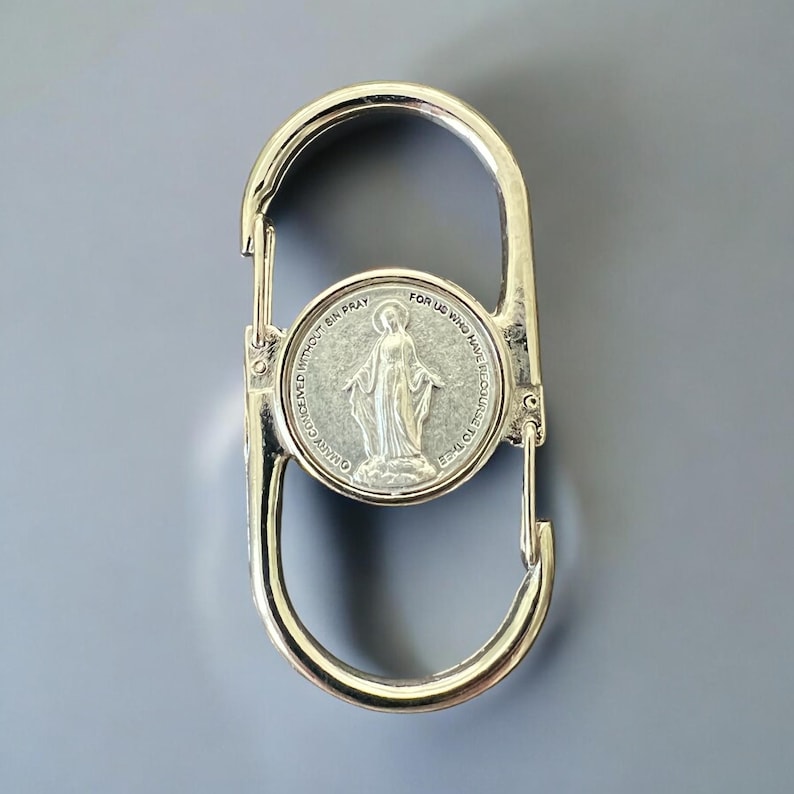 May include: Silver-toned metal keychain with a round charm featuring a depiction of the Virgin Mary. The charm has the text "OUR LADY CONCEIVED WITHOUT SIN PRAY FOR US WHO HAVE RECOURSE TO THEE" around the image.