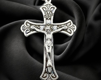 Può includere: Un crocifisso d'argento con un designo dettagliato e l'iscrizione "INRI" sul traverso. Il crocifisso è su uno sfondo di tessuto nero.
