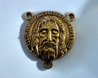 May include: A gold-toned metal religious charm featuring a relief image of Jesus' face with closed eyes and the inscription "ILLUMINA DOMINE VULTUM TUUM SUPER NOS".