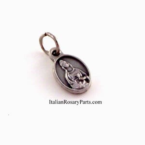 May include: Silver oval charm with a depiction of the Virgin Mary holding a baby Jesus. The charm has a loop for attaching to a necklace or bracelet.