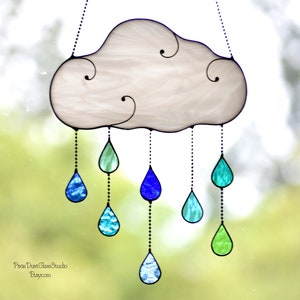 May include: A stained glass cloud with hanging teardrops. The cloud is white with black outlines and decorative swirls. The teardrops are various shades of blue and green, suspended by beaded chains.