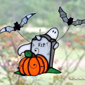May include: A stained glass Halloween suncatcher featuring a ghost, a pumpkin, a tombstone with the inscription "R.I.P.?", and two bats.