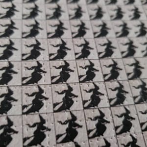 May include: A sheet of white paper with a repeating pattern of black witch silhouettes. Each witch is flying on a broomstick and has a pointed hat.