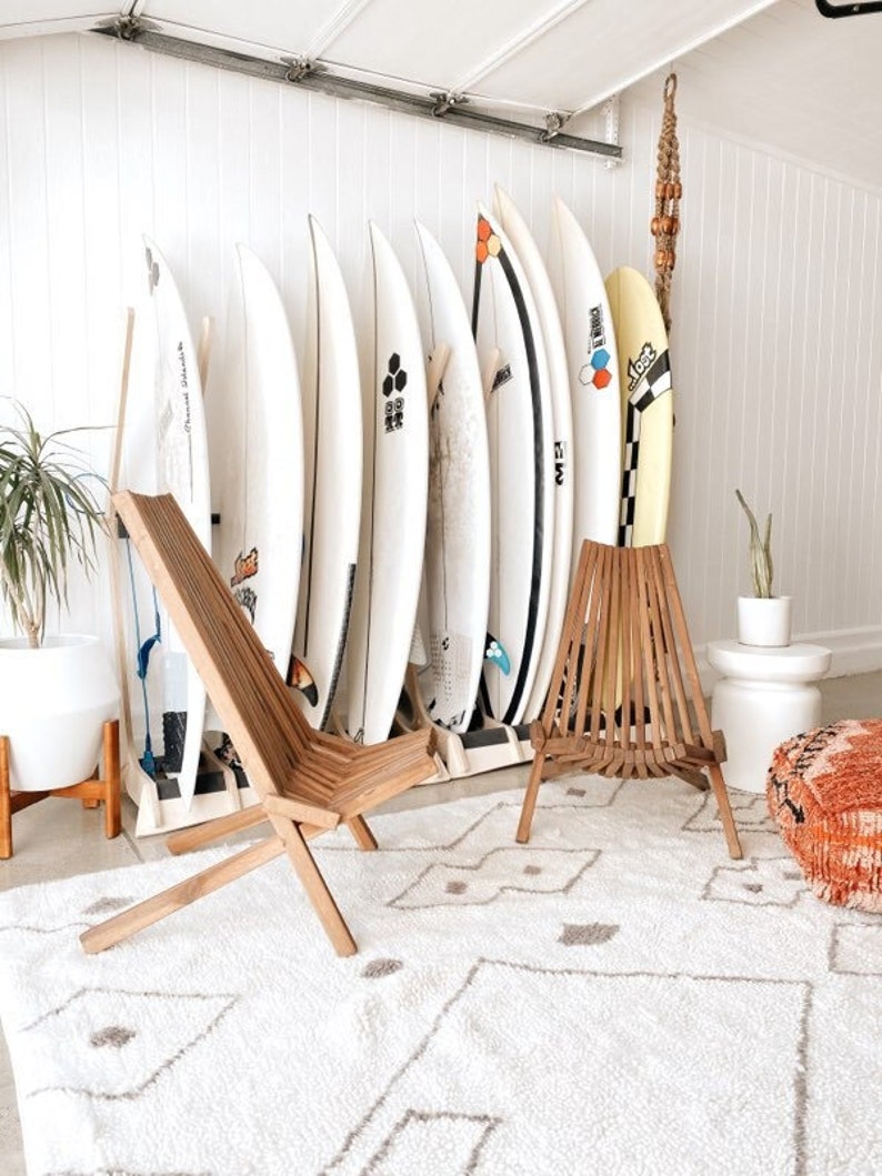Puede incluir: Dos sillas de madera con una alfombra de patr&oacute;n blanco y gris delante de una pared con tablas de surf. Las tablas de surf son blancas con dise&ntilde;os y logotipos coloridos.