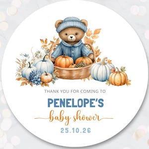 May include: A round sticker featuring a brown teddy bear in a blue hat and shirt sitting in a basket with pumpkins and autumn leaves. Text reads: THANK YOU FOR COMING TO PENELOPE'S baby shower 25.10.26. The design includes orange and white pumpkins.