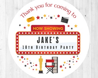 May include: Round white sticker with red and yellow movie marquee design. The marquee says "Now Showing Jake's 18th Birthday Party". The sticker has red, yellow, and black stars around the border.