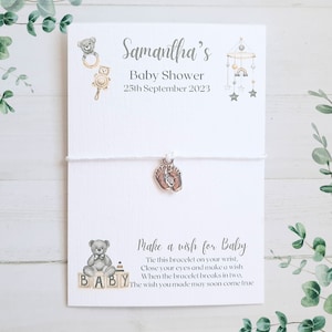 May include: A white string bracelet with a silver baby feet charm. The card attached to the bracelet says "Samantha's Baby Shower 25th September 2023" and "Make a wish for Baby Tie this bracelet on your wrist, Close your eyes and make a wish When the bracelet breaks in two, The wish you made may soon come true".