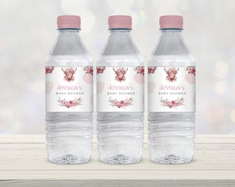 以下が含まれることがあります： ピンクのラベルが付いた透明なプラスチック製のウォーターボトルが3本。ラベルには、ハイランドカウの水彩画と花のアクセントが描かれています。ラベルのテキストは「ジェシカのベビーシャワー」です。
