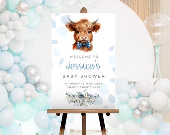 May include: A welcome sign for a baby shower with a blue and white watercolor background. The sign features a cartoon highland cow wearing a blue bow tie. The text on the sign reads "Welcome to Jessica's Baby Shower, Saturday 16th October, Twenty Twenty XXXX".