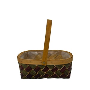 May include: A rectangular basket with a woven pattern in shades of green and burgundy. It has a wooden handle and a clear plastic liner. The basket is designed for carrying items.