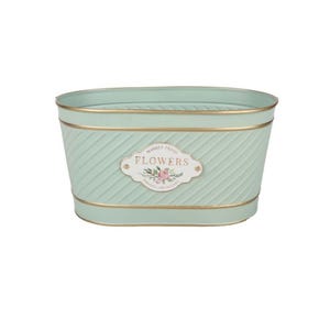 May include: A pale green metal planter with gold trim and a diagonal ribbed pattern. The oval-shaped planter features a label with the word "FLOWERS" and floral illustrations. The planter is designed for decorative use.