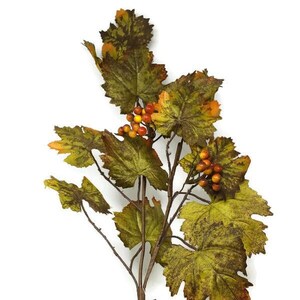 May include: A single stem of artificial autumn foliage with green and brown leaves and small orange and red berries. The stem is brown and has a tag attached to it that says "S&V ACC".