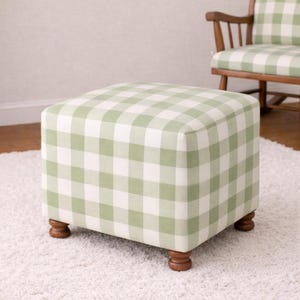 May include: A square ottoman with a green and white checkered pattern. The ottoman has a padded top and sits on four wooden, turned legs. A matching rocking chair is visible in the background.