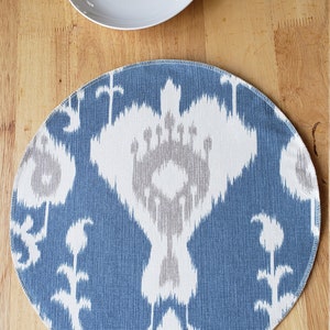 May include: A blue and white patterned placemat with a round shape. The placemat has a white border and a blue and white ikat design.