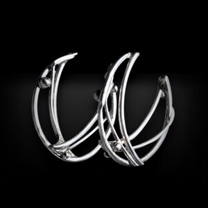 May include: A pair of silver hoop earrings with a geometric design. The earrings are made of thin wire and have small beads along the edges.