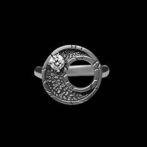 May include: A silver ring with a crescent moon design and a single clear diamond set in the center.
