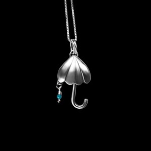May include: A silver necklace with a pendant shaped like an umbrella with a small turquoise bead hanging from it.