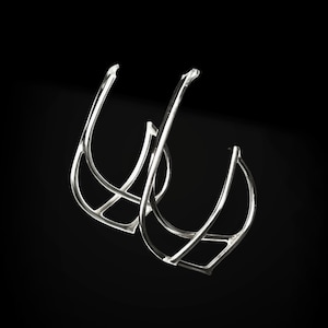 May include: A pair of silver hoop earrings with a geometric design. The earrings are made of thin metal and have a delicate, openwork pattern.