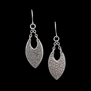 May include: A pair of silver dangle earrings with a textured, leaf-shaped design. The earrings have a delicate chain and a small loop at the top.