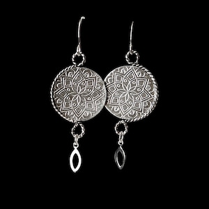May include: Silver earrings with a detailed mandala design and a dangling oval charm.