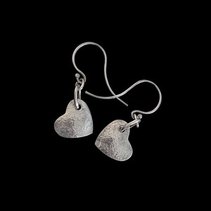 May include: A pair of silver heart-shaped earrings with a hammered texture and a simple hook closure.