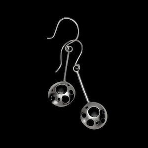 May include: A pair of silver dangle earrings with a circular design featuring multiple cut-out circles. The earrings have a simple, modern aesthetic.