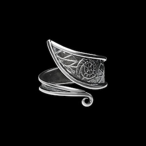 May include: A silver ring with a detailed, intricate design. The ring is open and wraps around the finger.