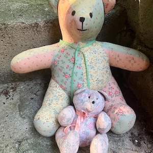 May include: A large and a small stuffed bear made from patchwork fabric featuring various floral patterns in shades of pink, yellow, green, and blue. The larger bear has a mint green ribbon around its neck, while the smaller bear has a pink ribbon.