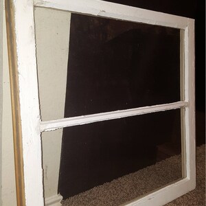 May include: White painted wood window frame with two panes of glass. The frame is slightly weathered and has a rustic look.
