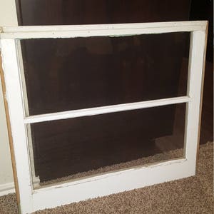 May include: A white painted wooden window frame with two panes of glass. The window is sitting on a brown carpet.