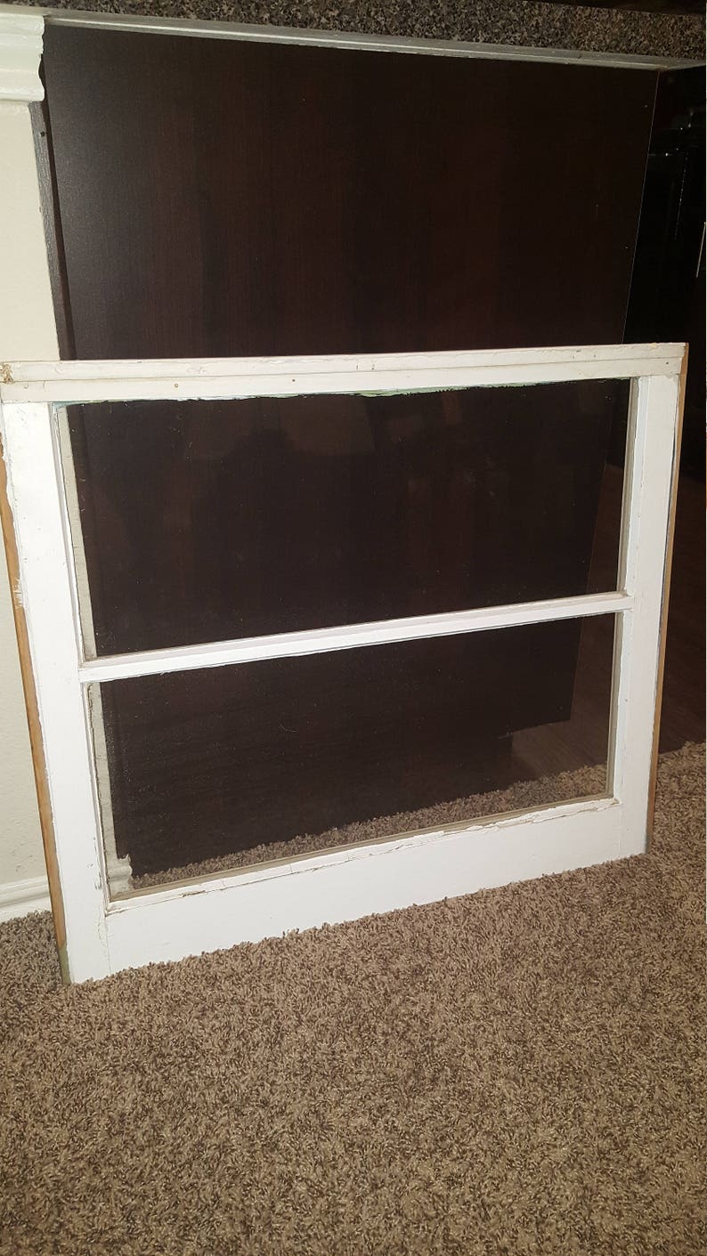 May include: A white painted wooden window frame with two panes of glass. The window is sitting on a brown carpet.