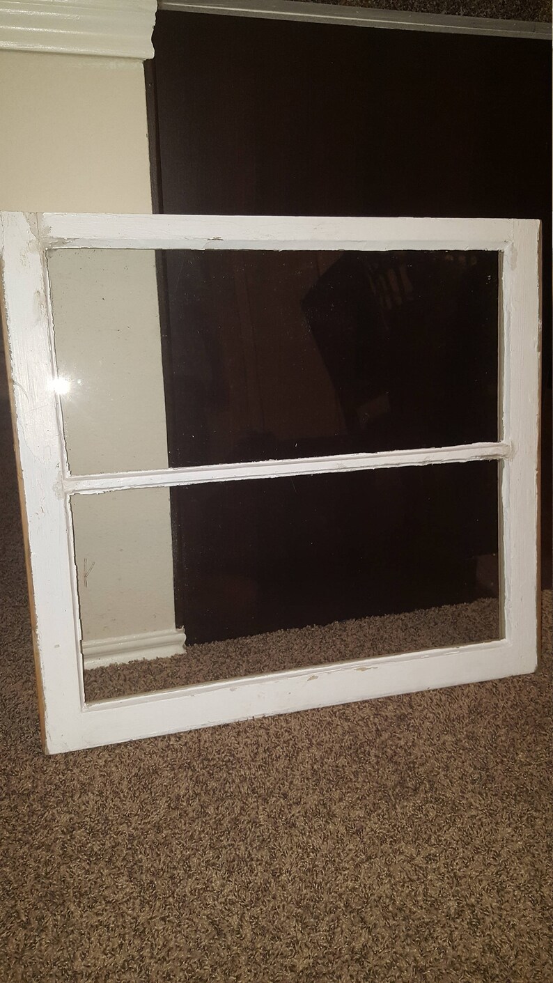 May include: A white painted wooden window frame with two panes of glass. The window is on a brown carpet.